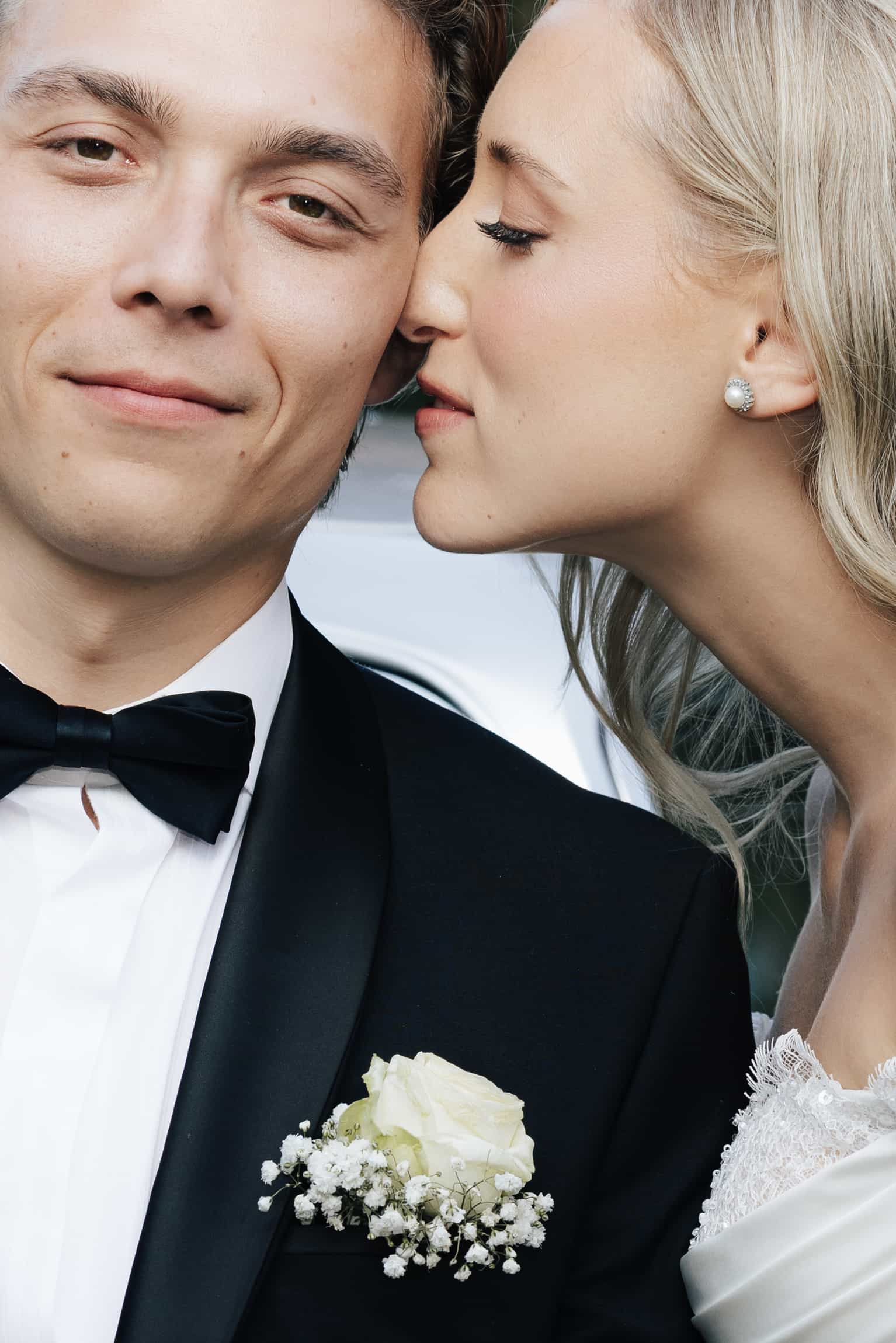 Braut im weißen Kleid mit zartem Strauß lehnt sich zum Kuss zum Bräutigam im Smoking, natürliche Farben