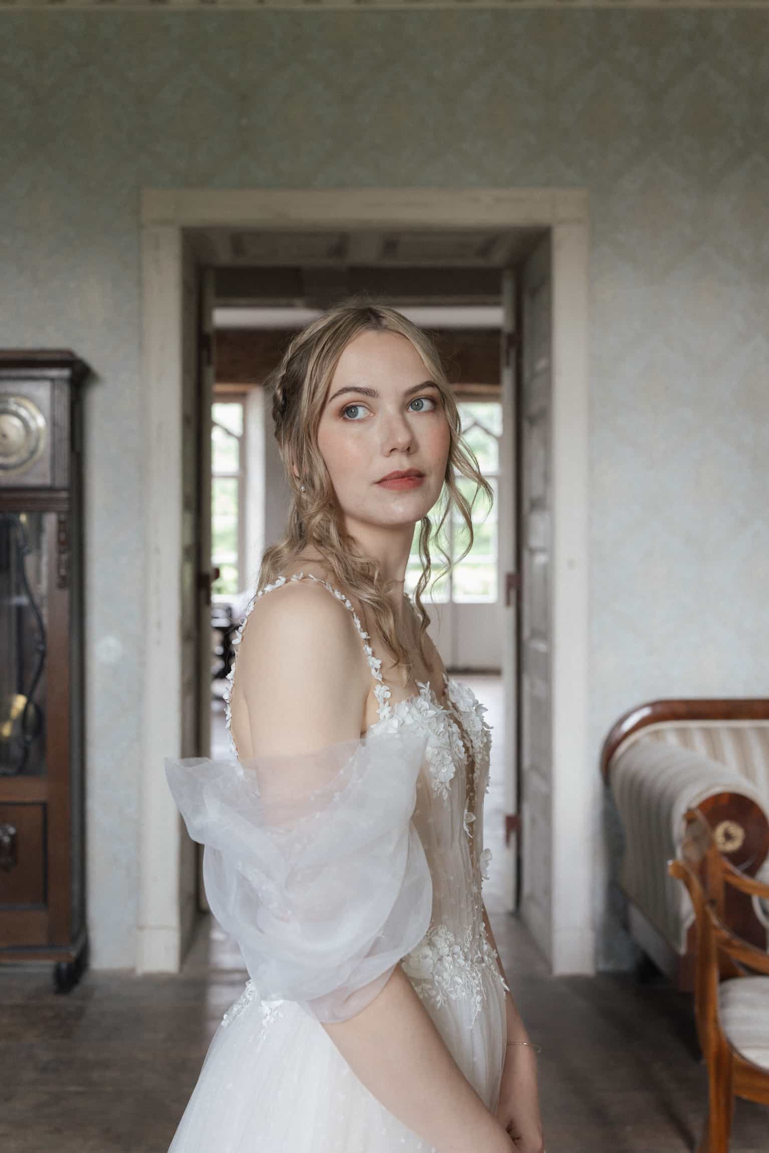 Braut in weißem besticktem Kleid mit Tüll-Cape, klassisches Interieur mit Türdurchblicken