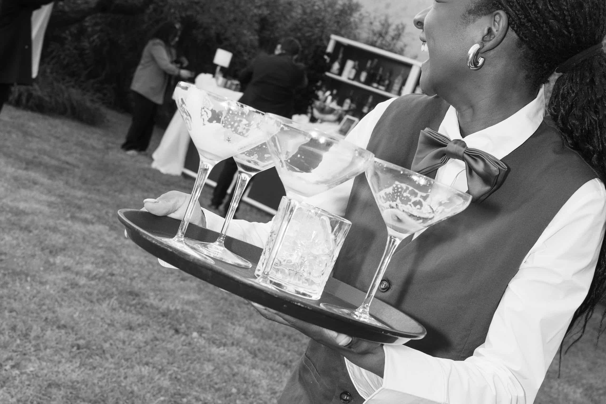 Service-Mitarbeiter mit Champagnergläsern beim Gartenempfang, reportageartige Schwarz-Weiß-Aufnahme