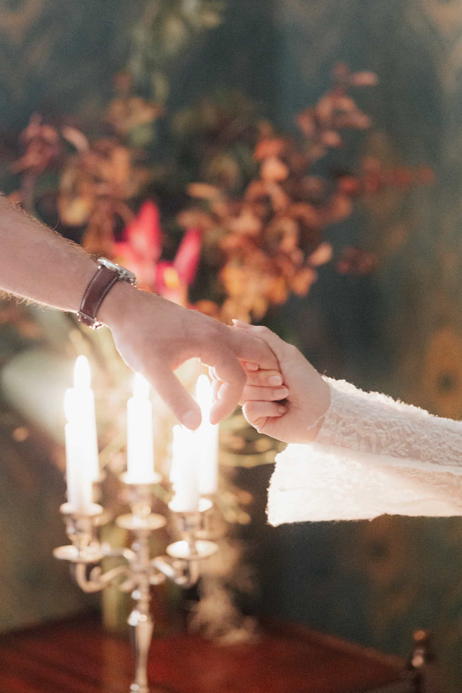 Hände mit Trauringen im Kerzenschein, unscharfe Hochzeitstafel dahinter