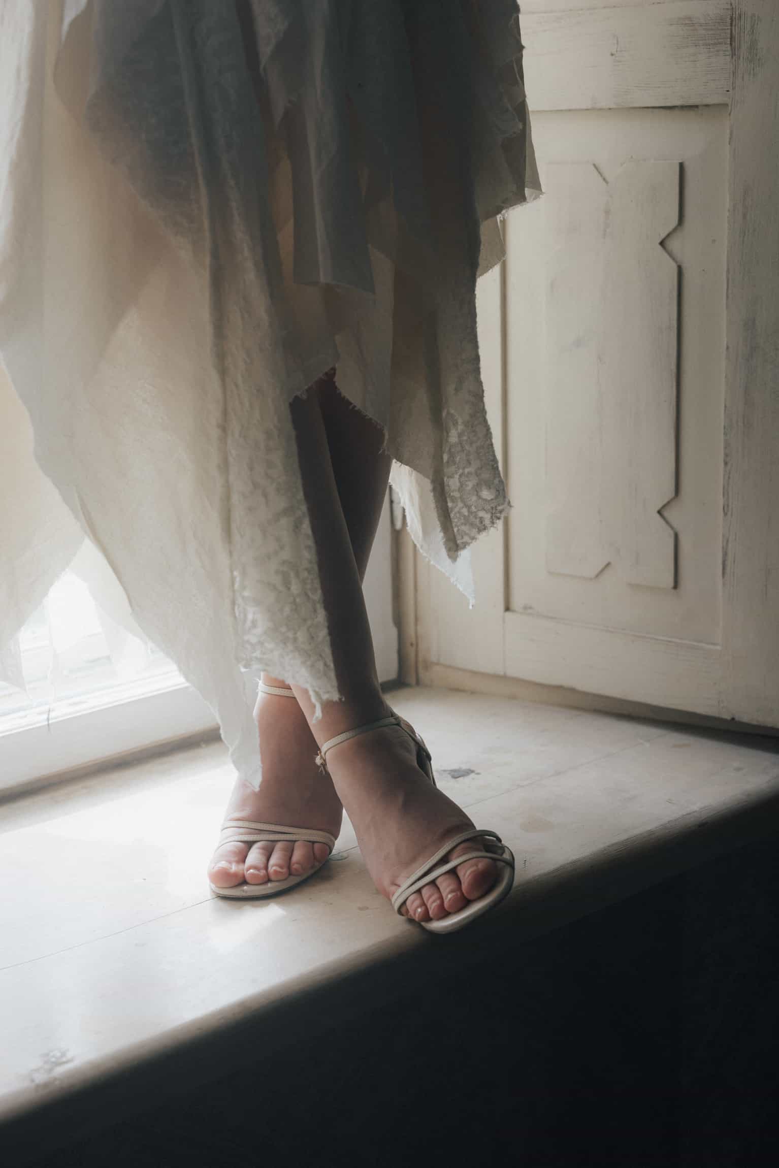 Detail: schwarze Sandalen unter einem weißen Hochzeitskleid auf einer sonnigen Schwelle