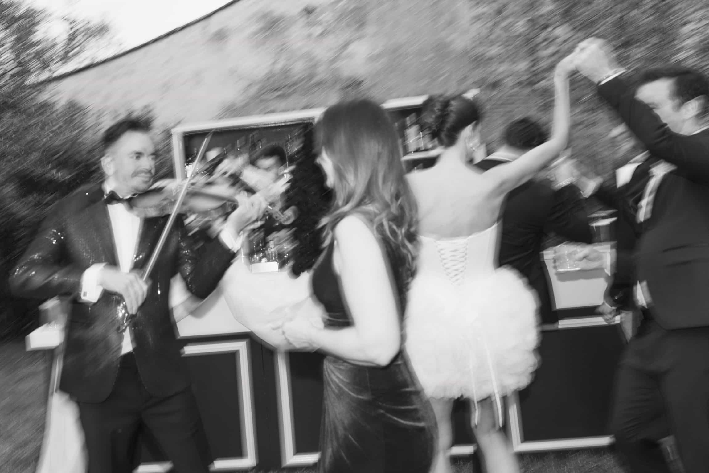 Black-and-white candid of bride dancing with motion blur, surrounded by formal wedding guests
