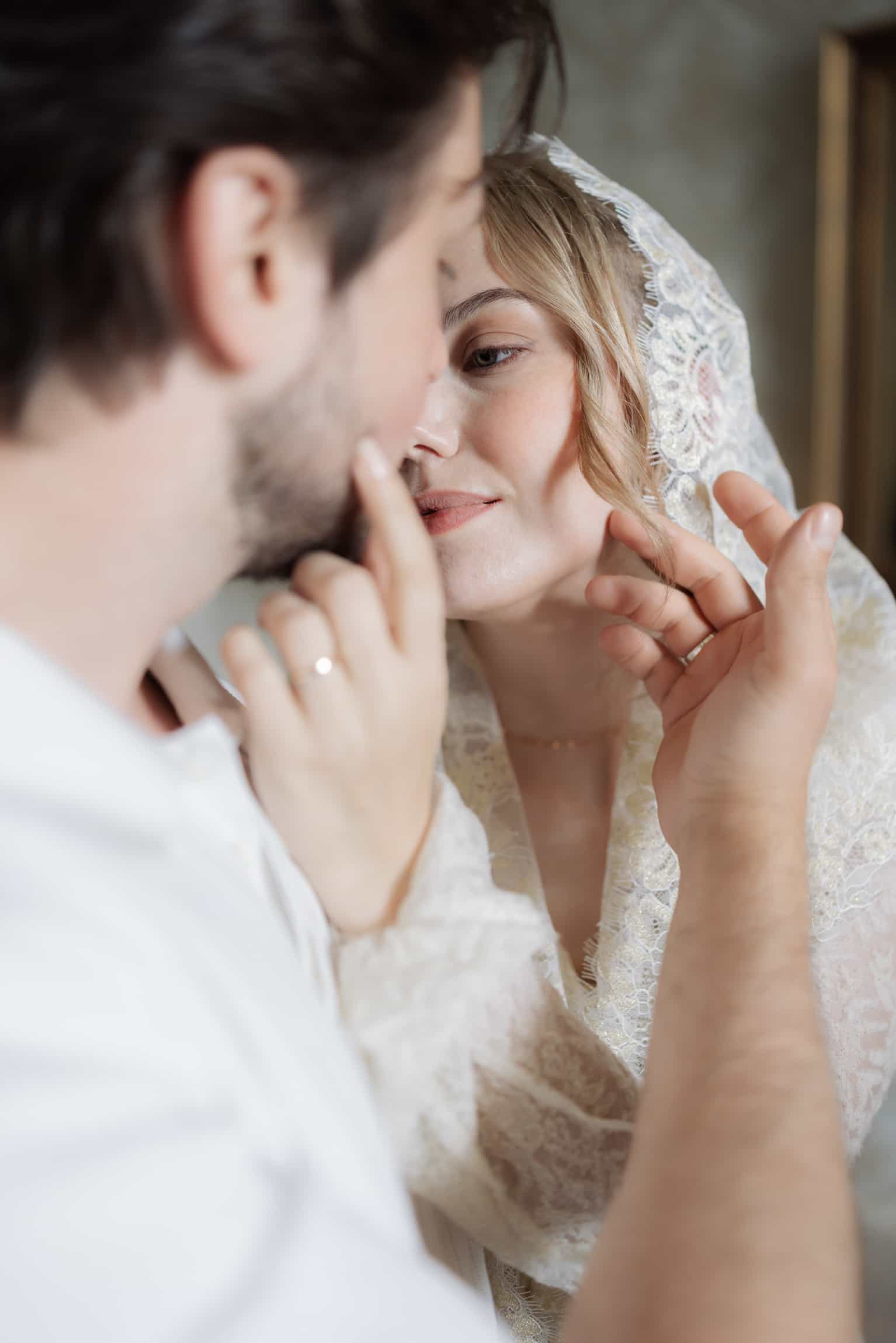 Close intimate moment between bride in veil and groom, gentle touch and eye contact