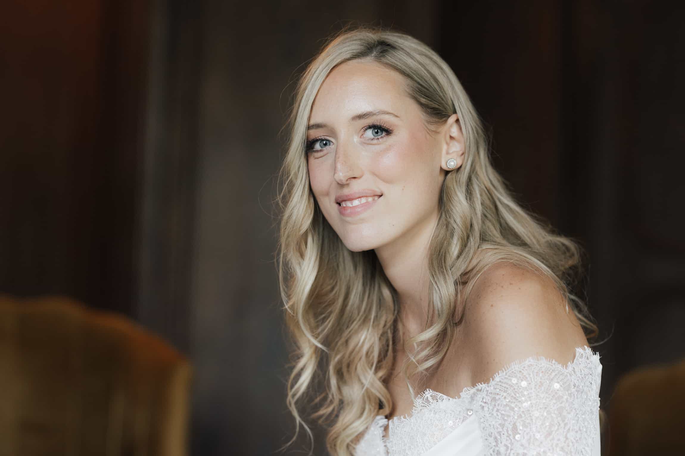 Bride looking over her shoulder with a gentle smile, wearing a white lace dress in soft warm light