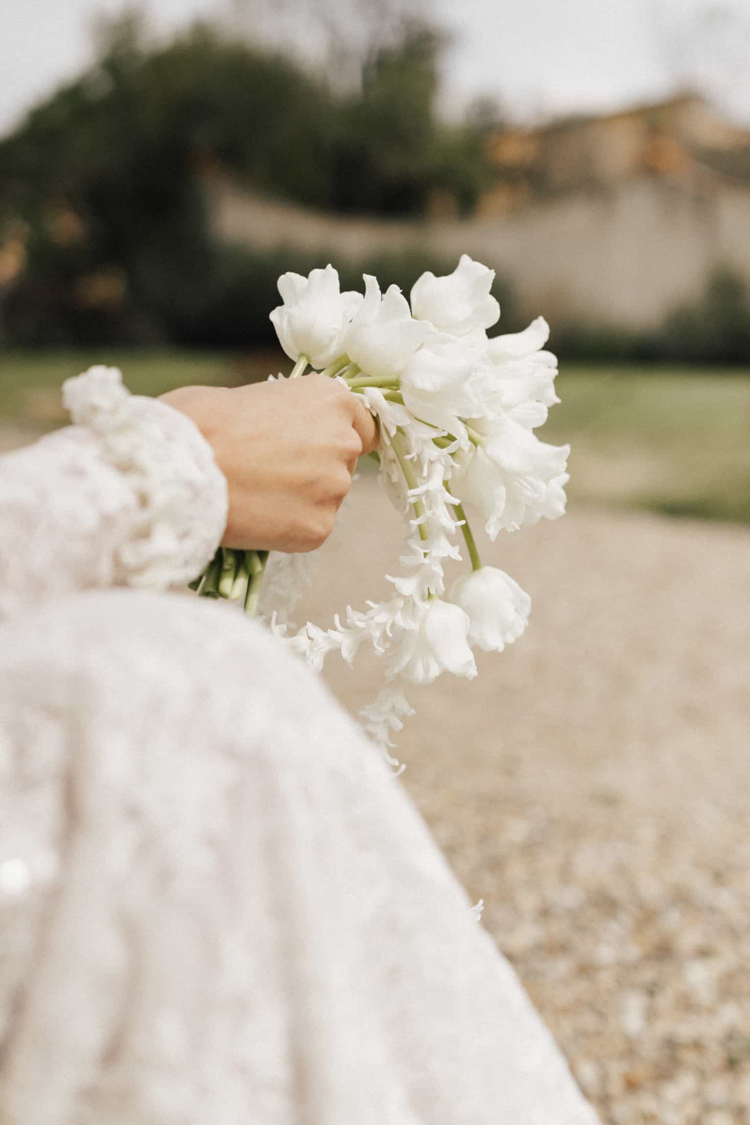 Bride in a white lace dress holding a large cascading white bouquet in a garden setting