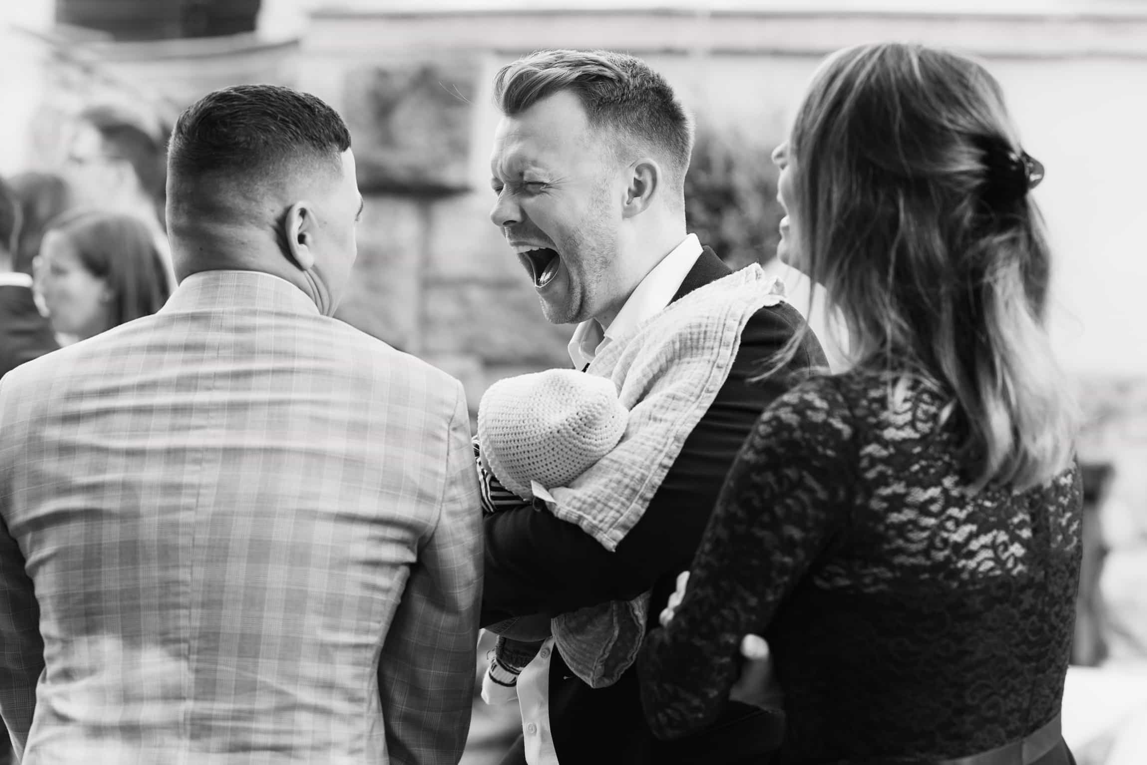 Candid black-and-white moment of groom laughing heartily with groomsmen at the wedding reception
