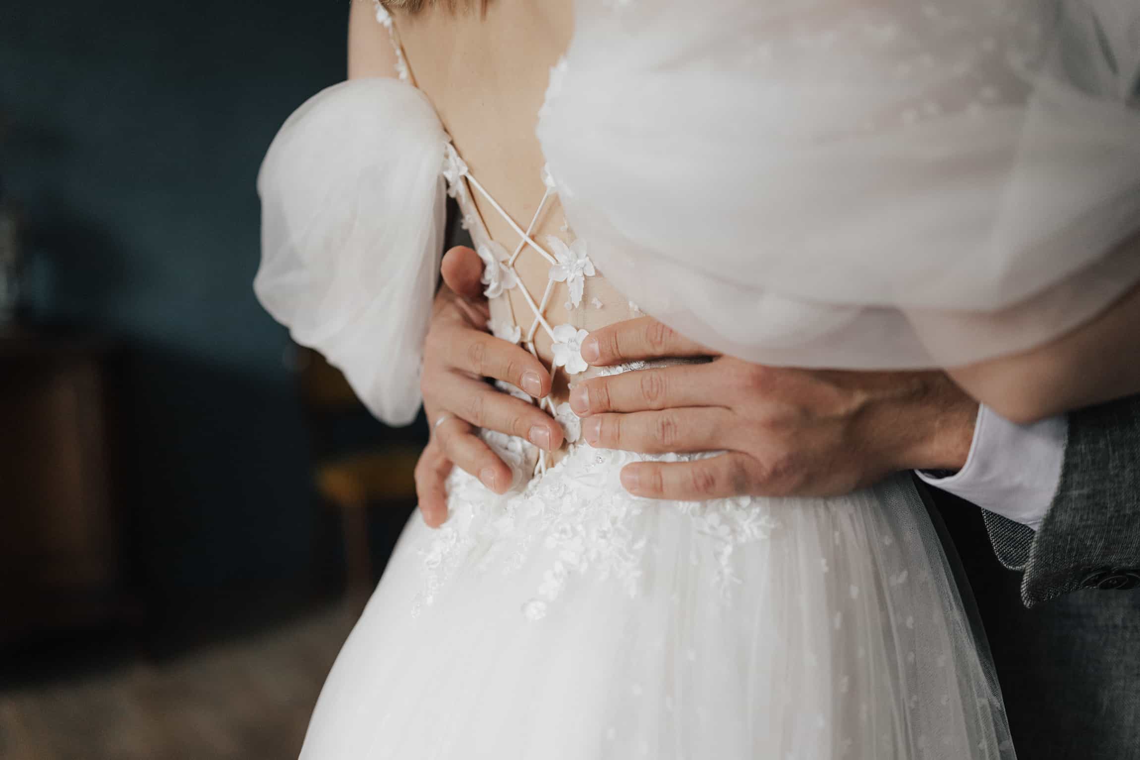 Close-up of groom's hands on bride's beaded lace wedding dress back, sensual wedding detail