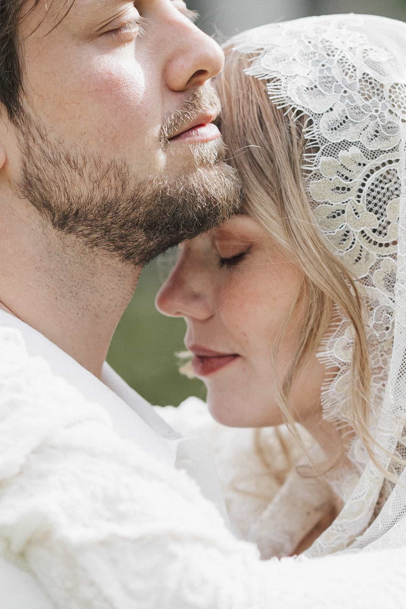 Close profile of bride in lace veil and groom nearly touching faces, intimate candid wedding moment