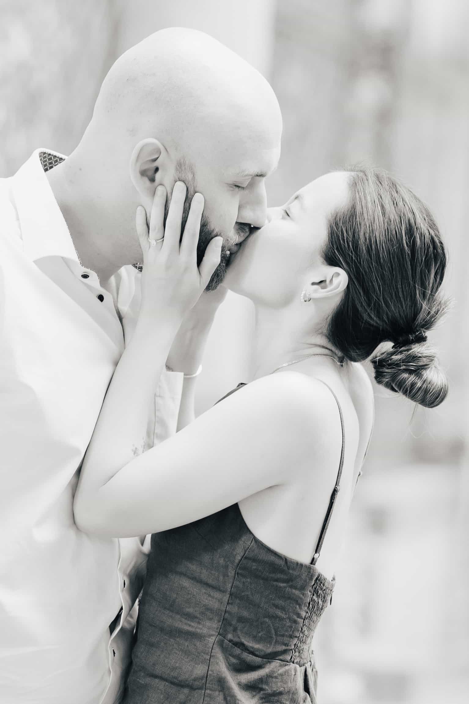 Black-and-white intimate portrait of bride and groom kissing tenderly, faces close, soft background