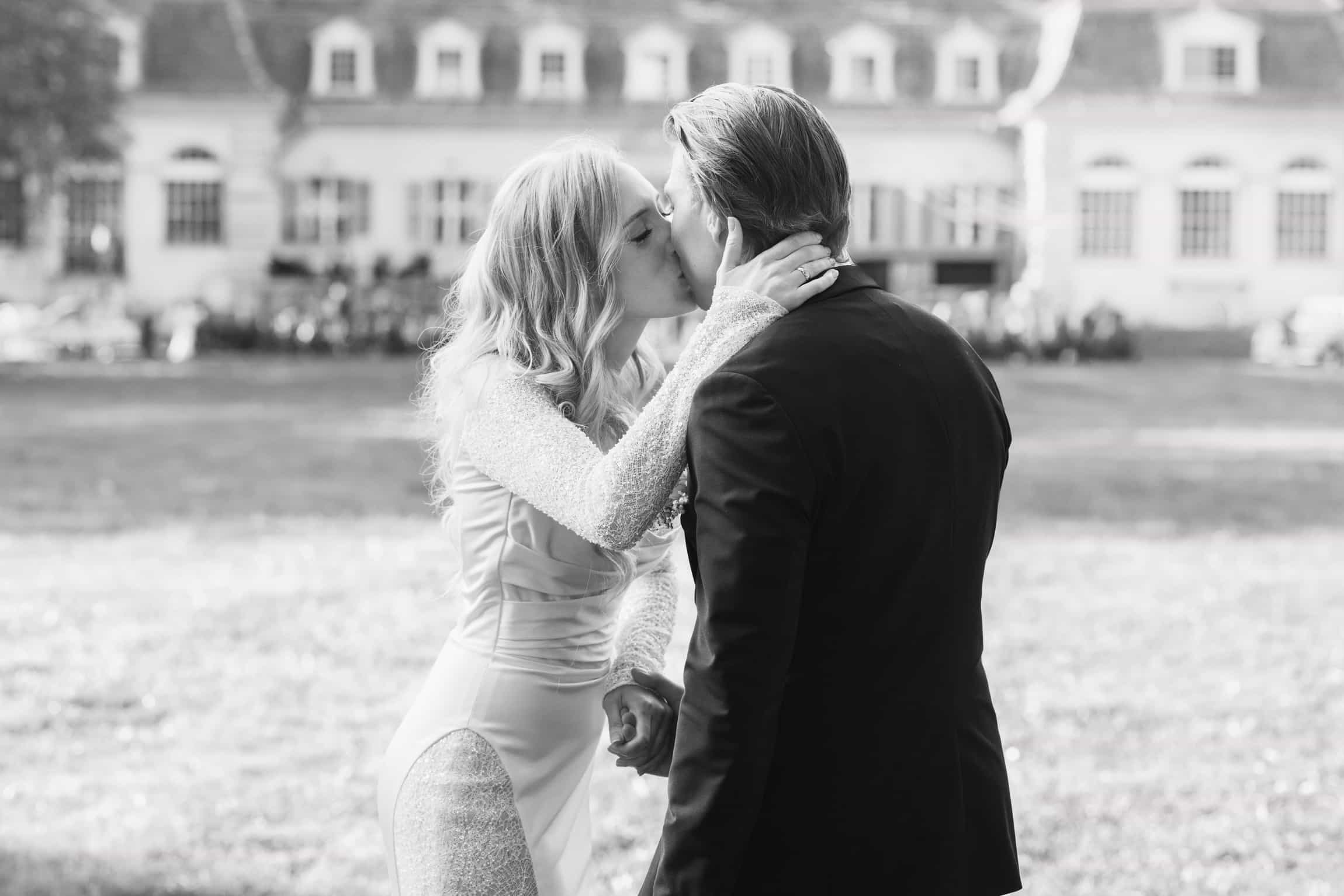 Bride and groom kissing outdoors in front of a white classical mansion with symmetrical windows