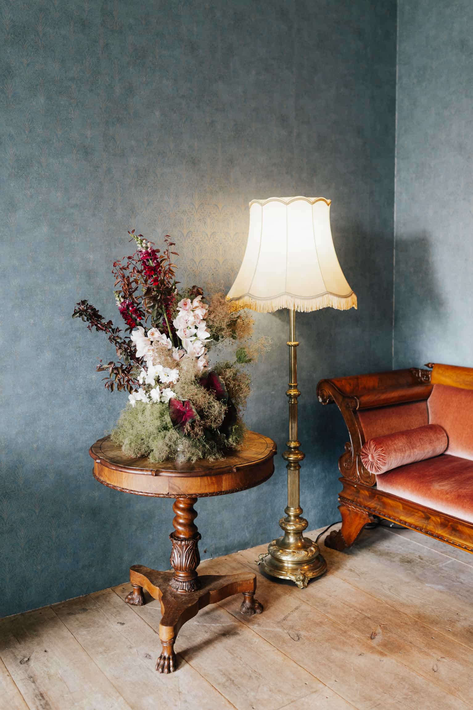 Styled interior with a wooden table, dried flowers in red and white, a brass floor lamp and a teal wall