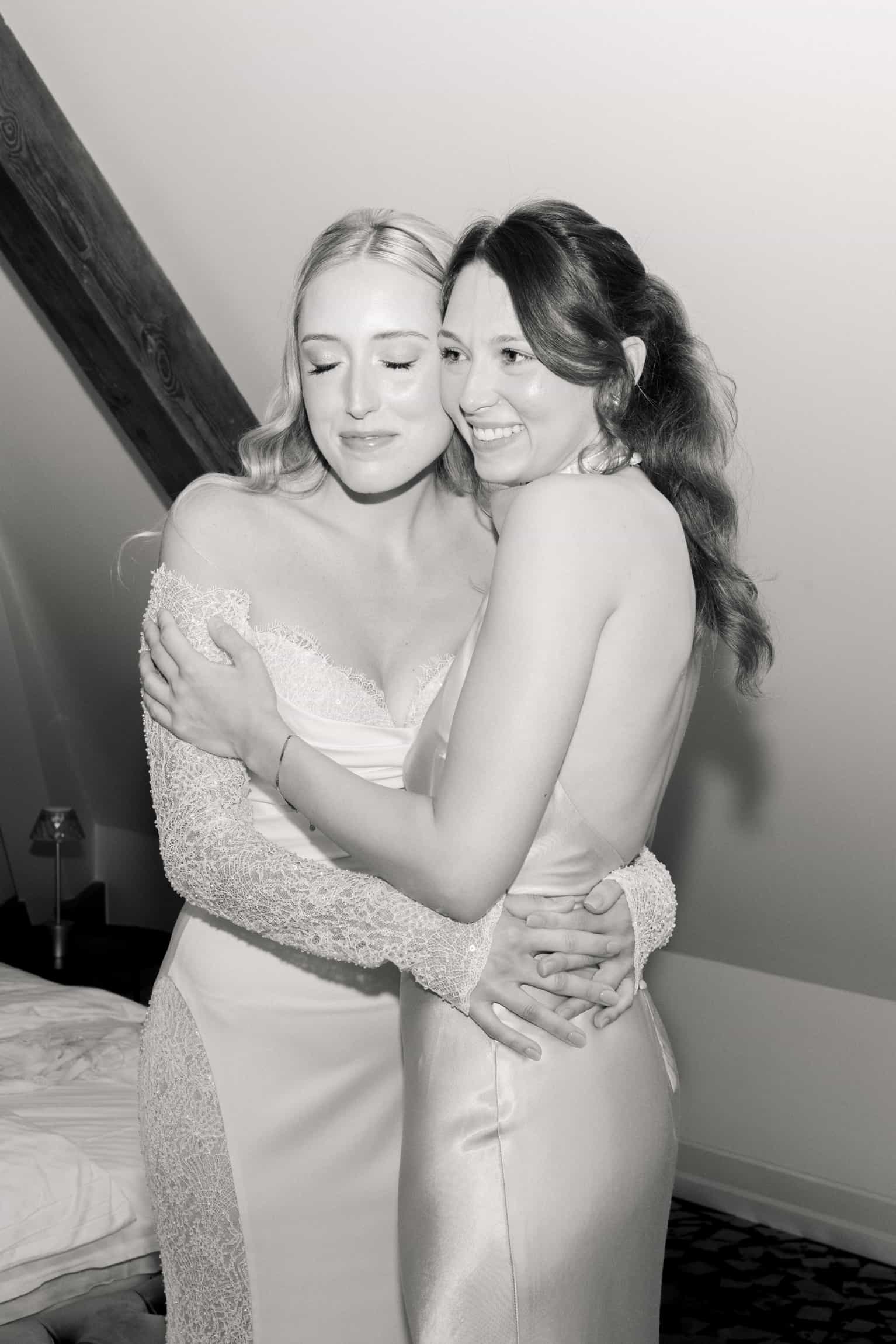 Two women in white wedding dresses embracing warmly, unposed black-and-white photograph